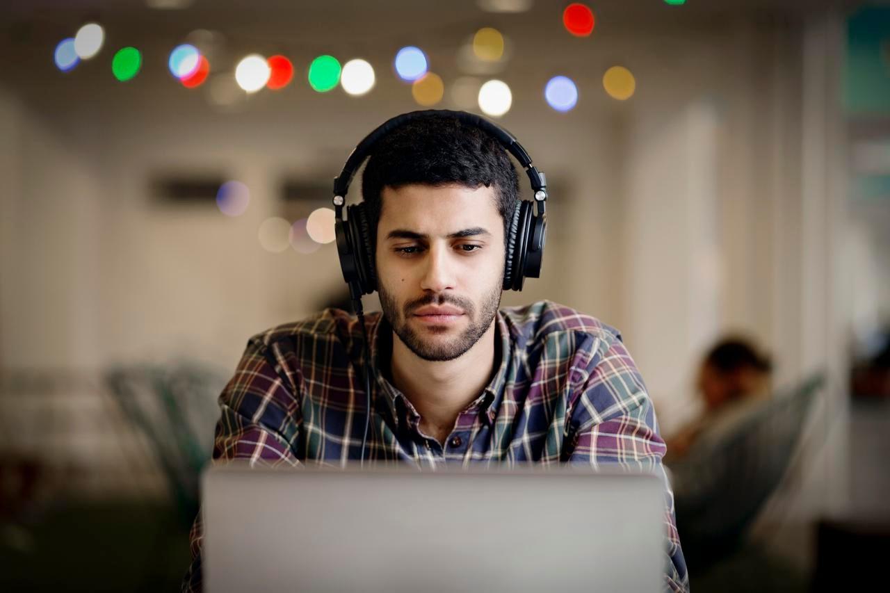  Businessman wearing headphones while working late on laptop in creative office クリエイティブ ・ オフィスのラップトップで遅くまで働いている間ヘッドフォンを身に着けているビジネスマン