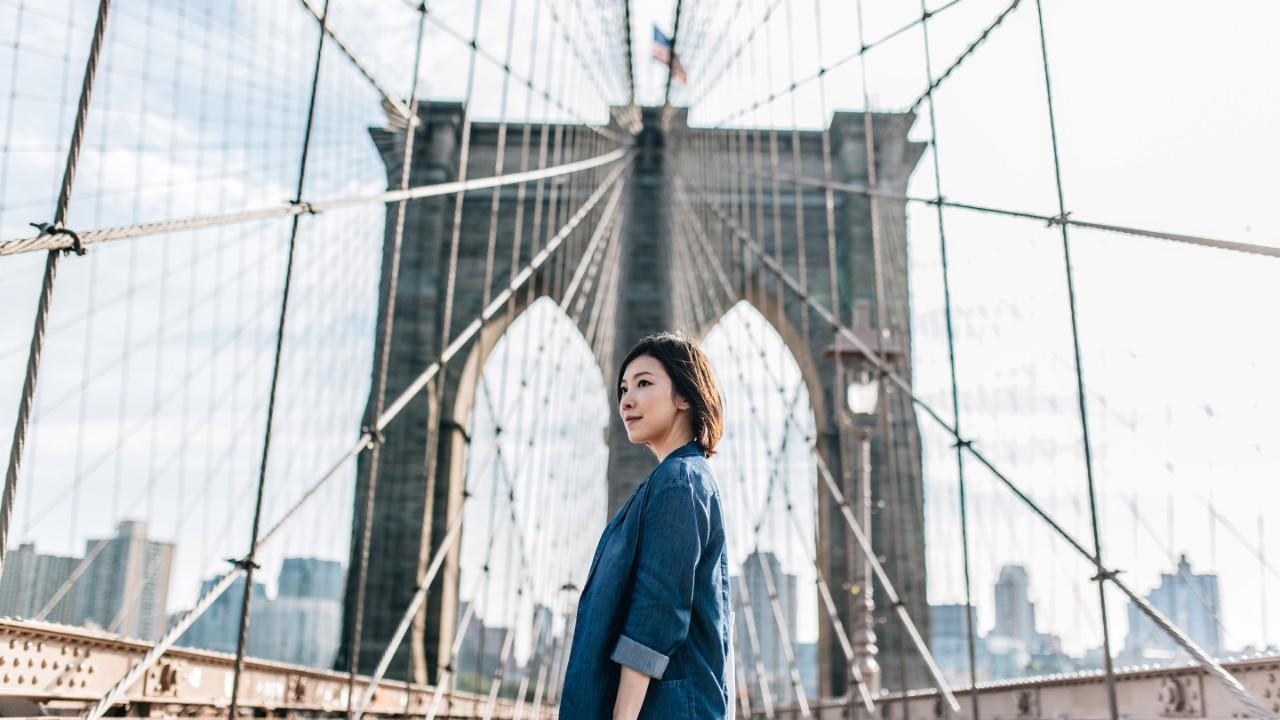 ブルックリン橋をニューヨークの街並みにそびえ立つ若いビジネスウーマン