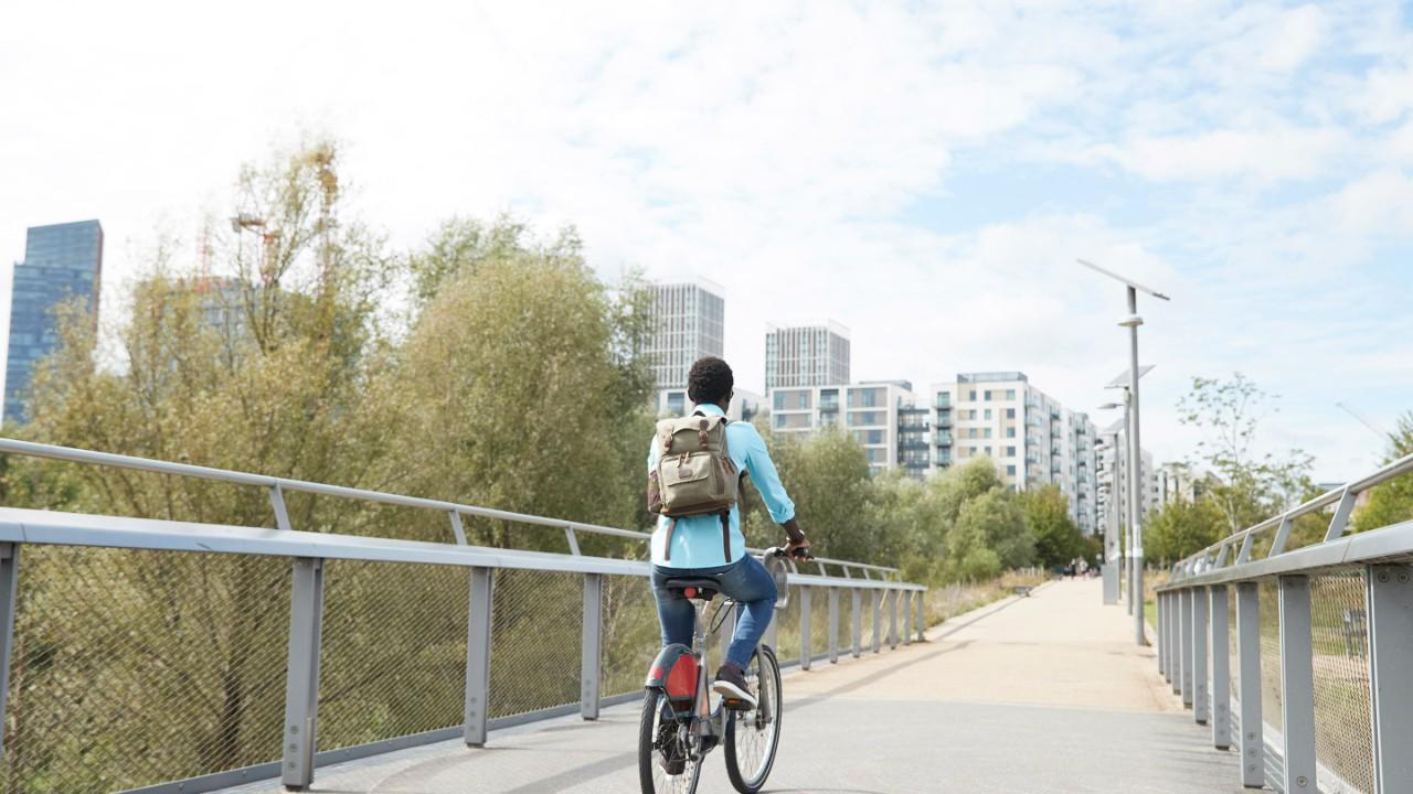 Rapariga a andar de bicicleta numa ponte em direção a uma cidade.